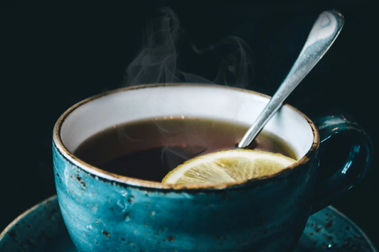 Blue mug of calming herbal tea with a lemon slice and a spoon on a saucer